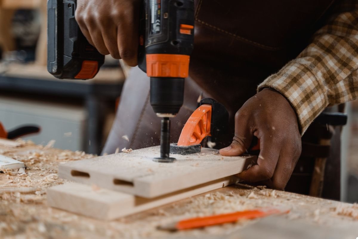 A man operates a drill to cut through a piece of wood, demonstrating woodworking skills and precision.